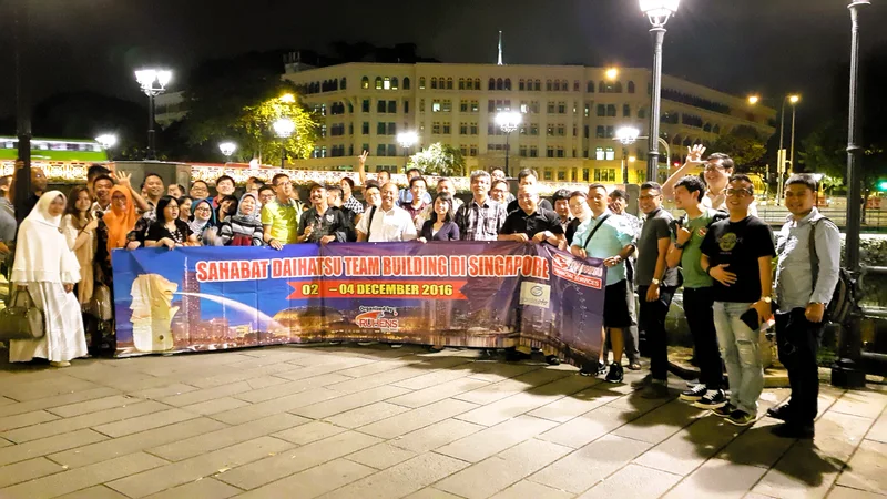 Grup perjalanan dengan spanduk Sahabat Daihatsu berfoto di Singapura pada malam hari.
