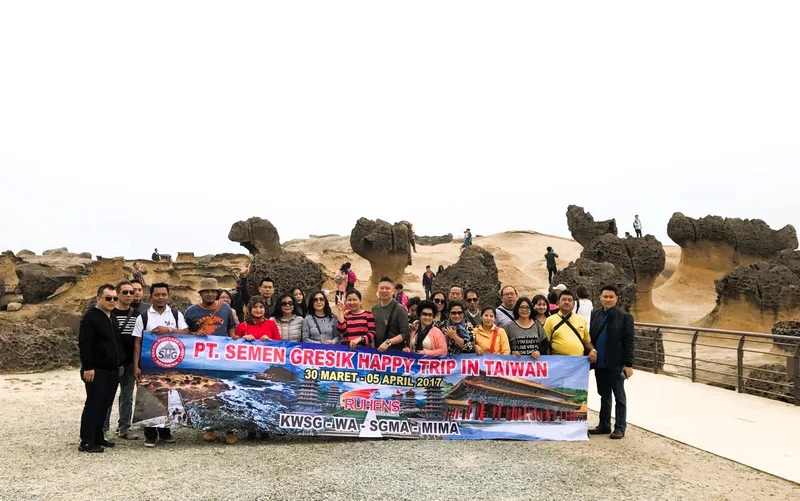 Grup perjalanan dengan spanduk Semen Gresik berfoto di depan formasi batu di Taiwan.
