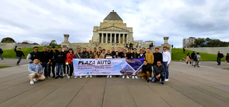 Grup perjalanan Ruhens berfoto dengan spanduk di depan monumen batu di Australia.