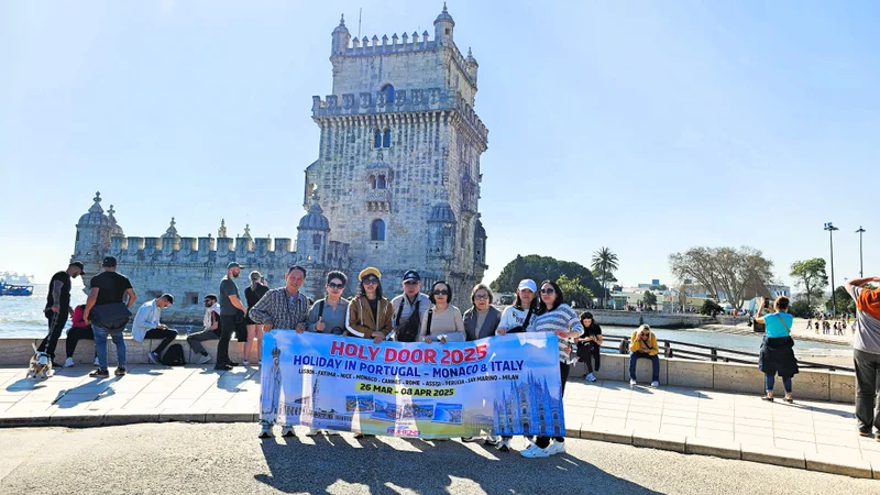 Grup perjalanan dengan spanduk Holy Door berfoto di depan menara batu di tepi perairan Portugal.