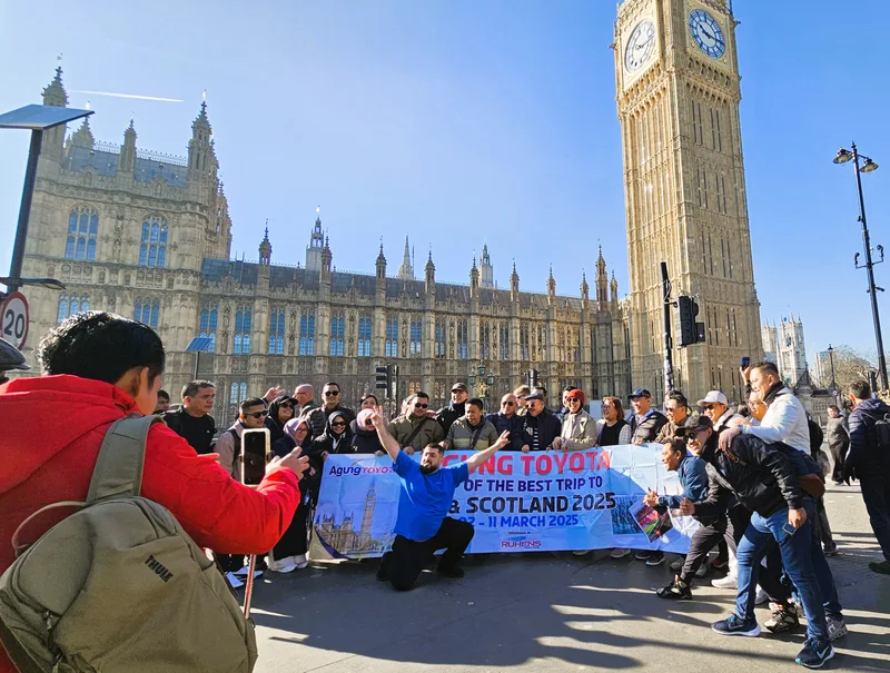 Grup perjalanan dengan spanduk Agung Toyota berfoto di depan gedung parlemen dan menara jam di London.